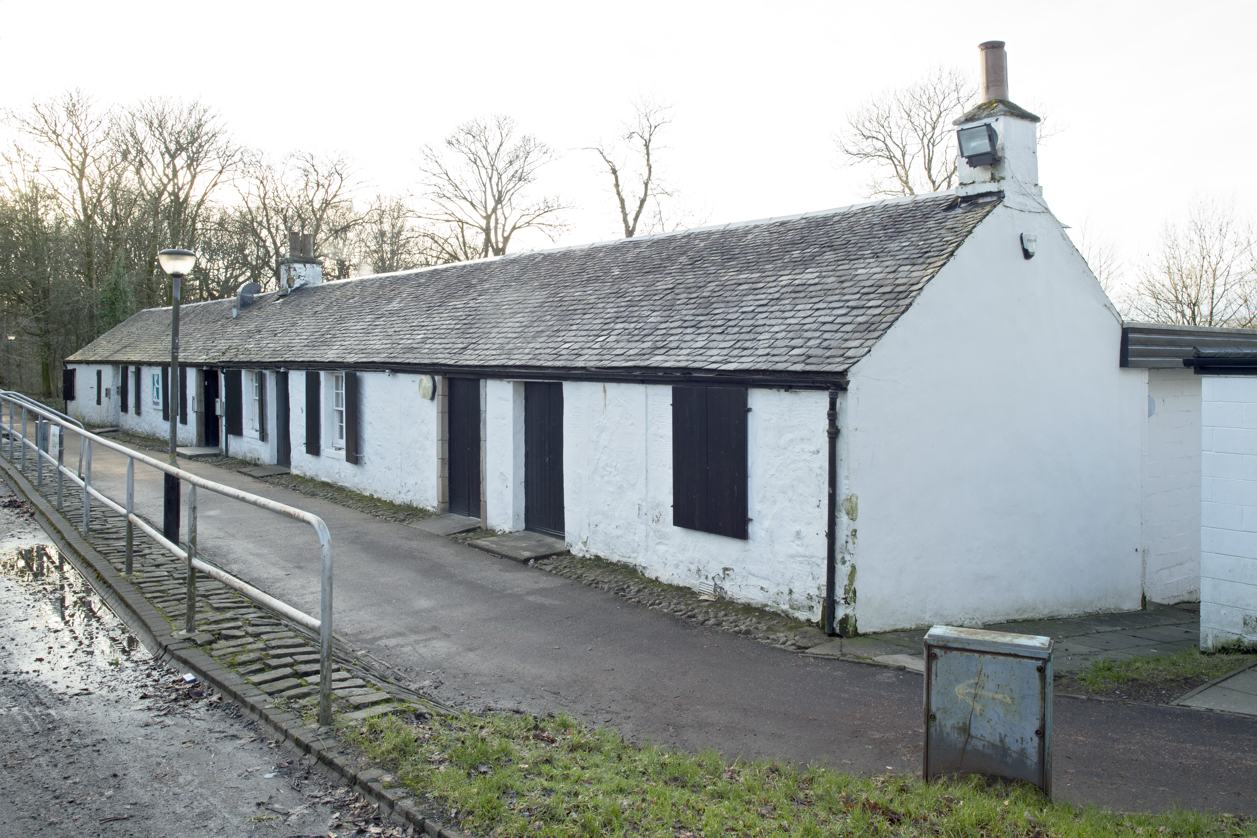 White row of cottages, grey roof, black boarded doors and shutters, white sky with trees
